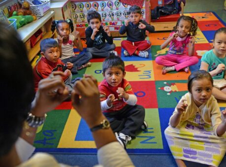 A group of 5-year-old children sit in a circle and sing with a teacher