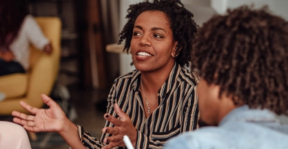 A seated woman speaks and gestures with her hands in an indoor space.