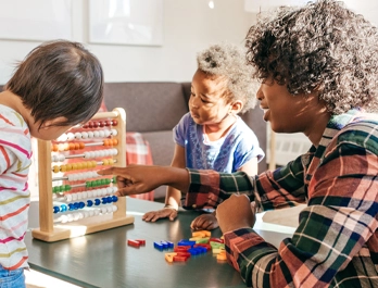 A woman shows two toddlers the colored beads of an abacus