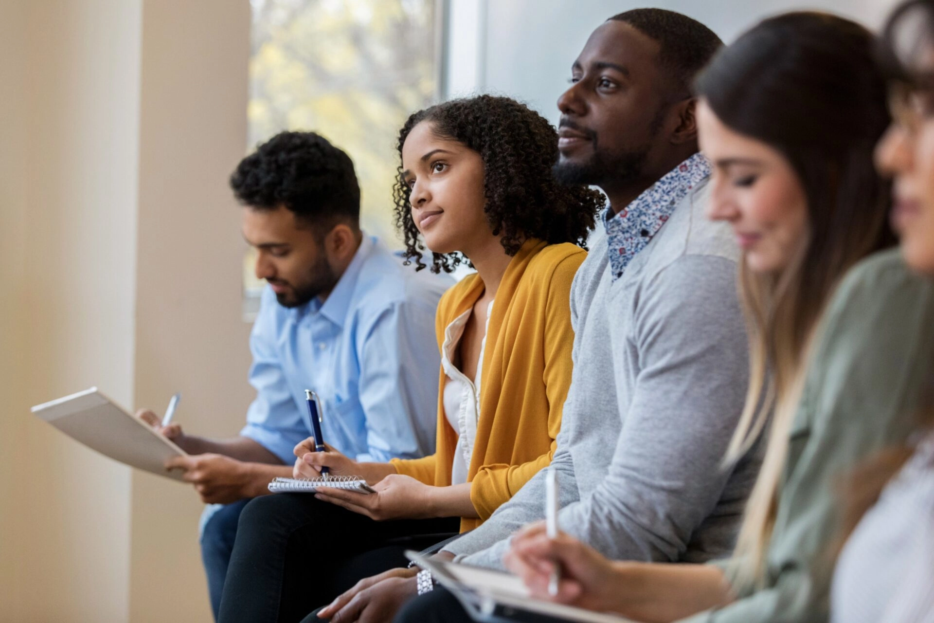 A group of people in an audience are focused and taking notes.