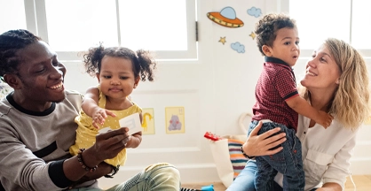 A man and a woman are seated on the floor, holding a toddler boy and toddler girl.