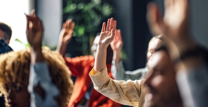 Multiple people in an audience raise a hand.