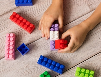 A child's hands fit colorful LEGO blocks together on a wooden table.