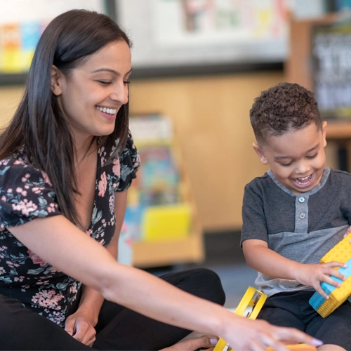 A woman and a young boy play with blocks anda tambourine together.