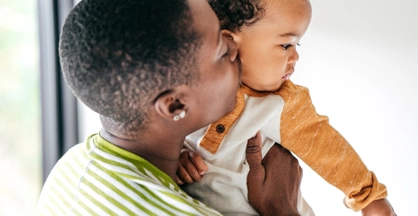 An adult holds an infant and kisses the child's cheek