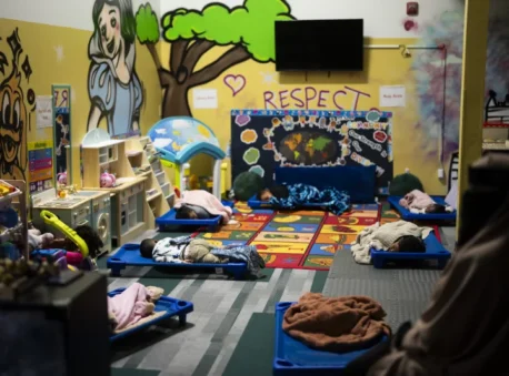 Children sleep on cots in a preschool room with colorful murals on the walls.